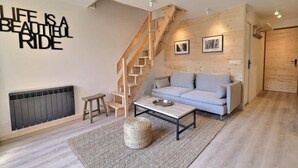 A modern living room with a wooden staircase, a grey sofa, a coffee table, and a wall with a motivational quote. - 10m from ski slopes, 4th floor, 62m², Méribel-Mottaret (Méribel - Les Allues)