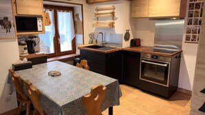 A compact kitchen with a dining table, wooden chairs, a built-in oven, and a stainless steel refrigerator. - Chalet, fireplace or stove, tv, 62m², Pralognan-la-Vanoise (Pralognan-la-Vanoise)