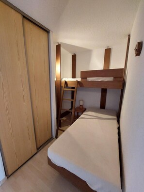 Een kleine slaapkamer met een stapelbed, een houten garderobe en een bureau met een stoel.