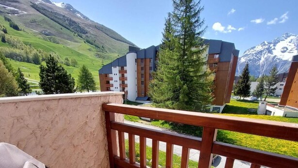 A balcony with a wooden table and two chairs, overlooking a mountainous landscape and modern buildings. - 50m from resort center, 3rd floor, view mountain, balcony, tv, 52m², Les 2 Alpes (Les Deux Alpes)