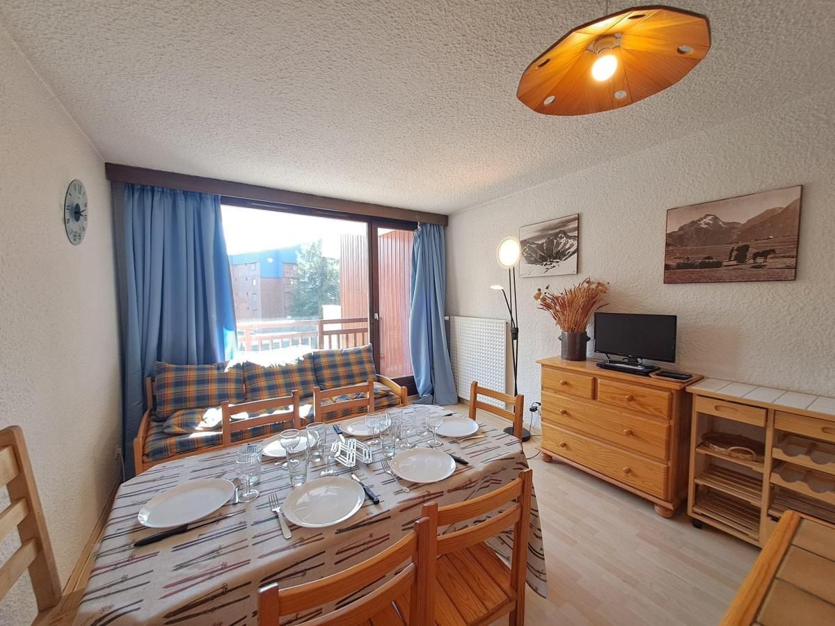 Zona pranzo con tavolo apparecchiato per quattro persone, televisione su un mobile in legno e finestra con tende.