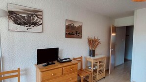 A room with a wooden dresser, a desk, and two chairs. There are two wall-mounted pictures depicting landscapes. - 50m from resort center, 3rd floor, view mountain, balcony, tv, 52m², Les 2 Alpes (Les Deux Alpes)