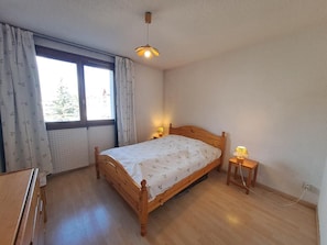 Een slaapkamer met een houten bed, een nachtkastje met een lamp, een raam met gordijnen en een radiator.