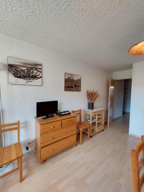A room with a wooden dresser, a desk, and two chairs. There are two wall-mounted pictures depicting landscapes.