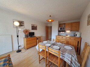 Een kleine keuken met houten kastjes, een eettafel voor vier personen en een kleine koelkast.