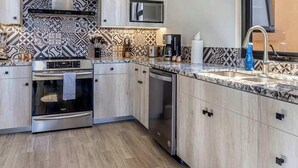 Une cuisine moderne avec des meubles de couleur bois clair, un crédence à motifs, des appareils électroménagers en acier inoxydable et une grande fenêtre.