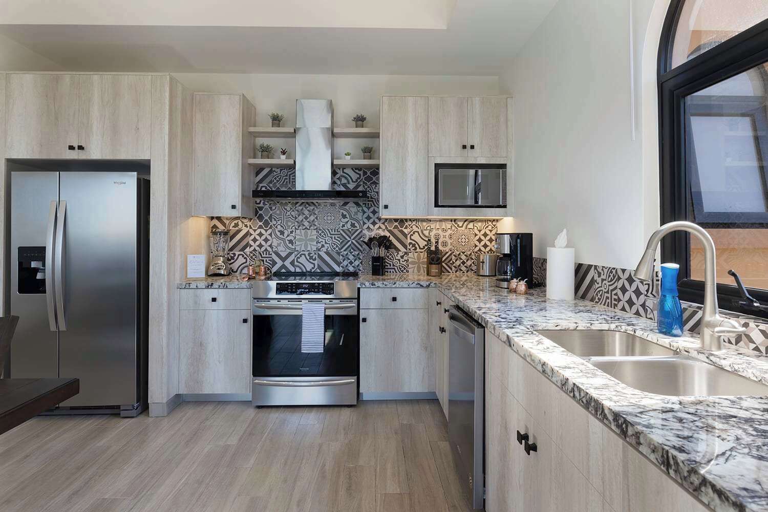 Une cuisine moderne avec des meubles en bois clair, des appareils en acier inoxydable et un pare-feu décoratif.