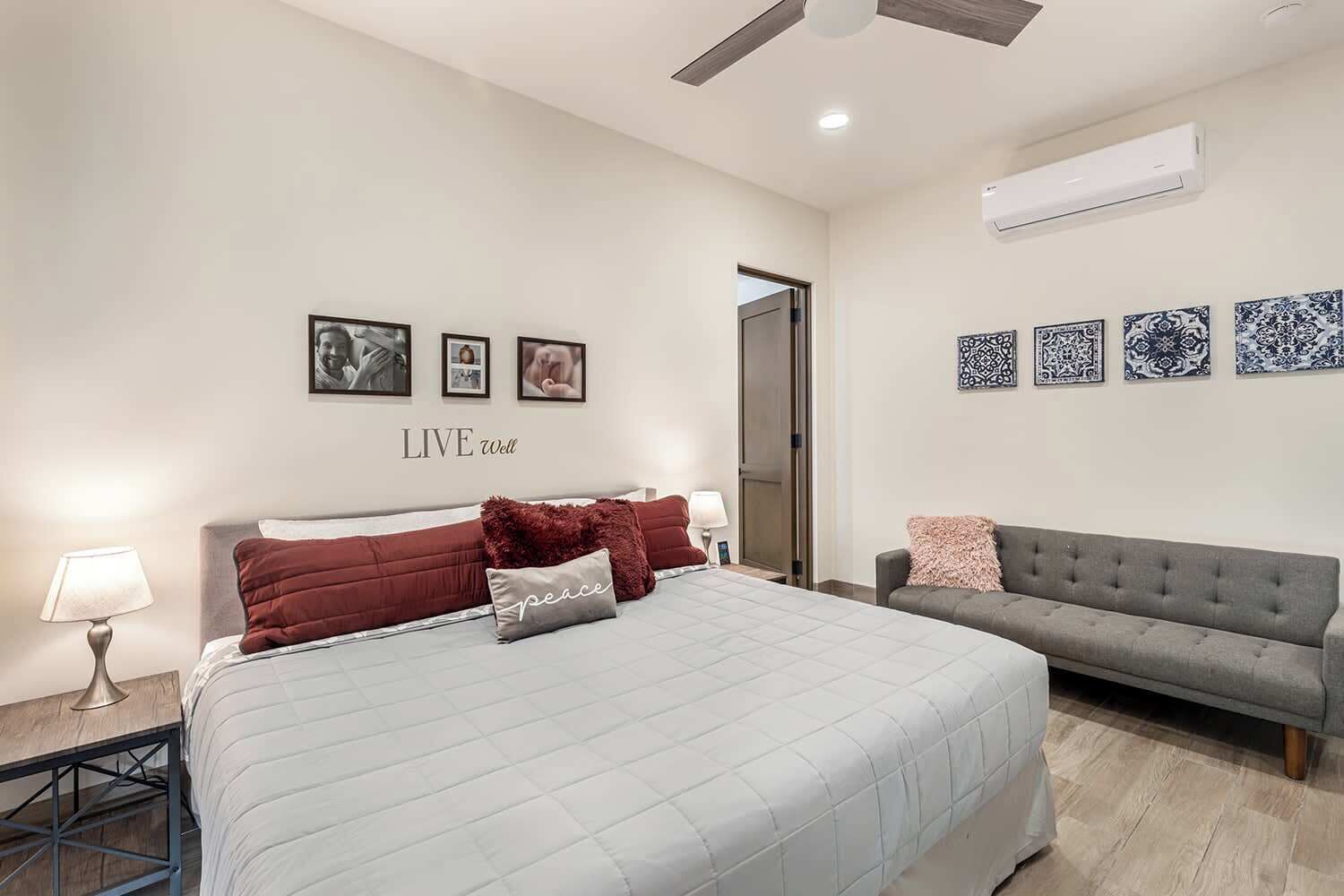 A bedroom with a bed, a grey sofa, and a wall with framed pictures.