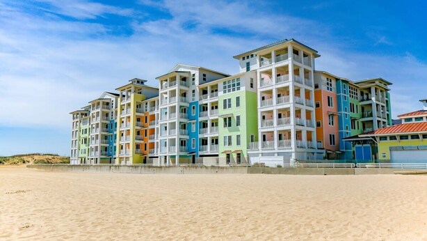 Un hotel de varios pisos con balcones, situado junto a una playa de arena.