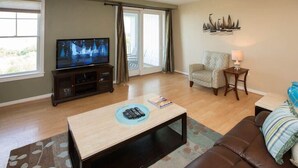 Una sala de estar con televisor, sofá, sillón, mesa de centro y lámpara.
