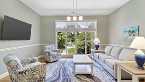 A living room with a sofa, two armchairs, a coffee table, and a TV mounted on the wall.
