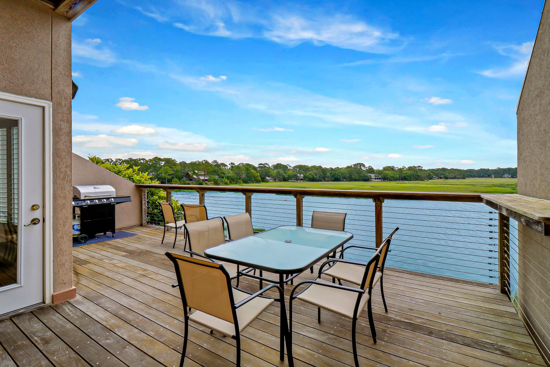 A deck with a table and chairs, overlooking a body of water and a park.