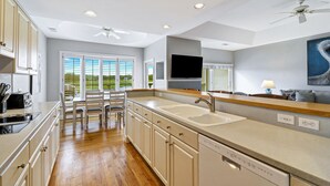 A modern kitchen with a central island, built-in appliances, and a large window with blinds.