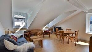 A loft-style living area with a high ceiling, wooden flooring, a sofa with a fur throw, a dining table with chairs, and a view of a house through a skylight. - Le Refuge, Chamonix Centre (Chamonix-Mont-Blanc)