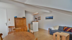 A spacious living area with a wooden dining table and chairs, a gray sofa with colorful cushions, and a kitchen in the background. - Le Refuge, Chamonix Centre (Chamonix-Mont-Blanc)