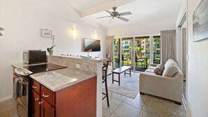A modern kitchen with a central island, a dining area with a sofa and table, and a balcony with curtains. - Kailani #314, Top Floor, Walk to Kapaa Town and Beach (Kapaa)
