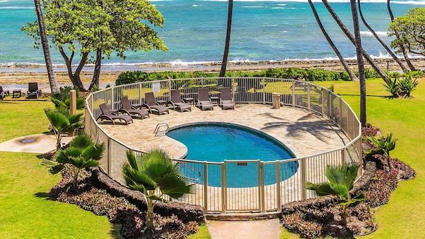 A circular pool with a surrounding deck, palm trees, and a view of the ocean. - Kailani #314, Top Floor, Walk to Kapaa Town and Beach (Kapaa)
