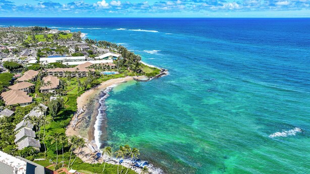 Un complejo turístico frente al mar con propiedades en la playa, aguas turquesas cristalinas y vistas al océano.