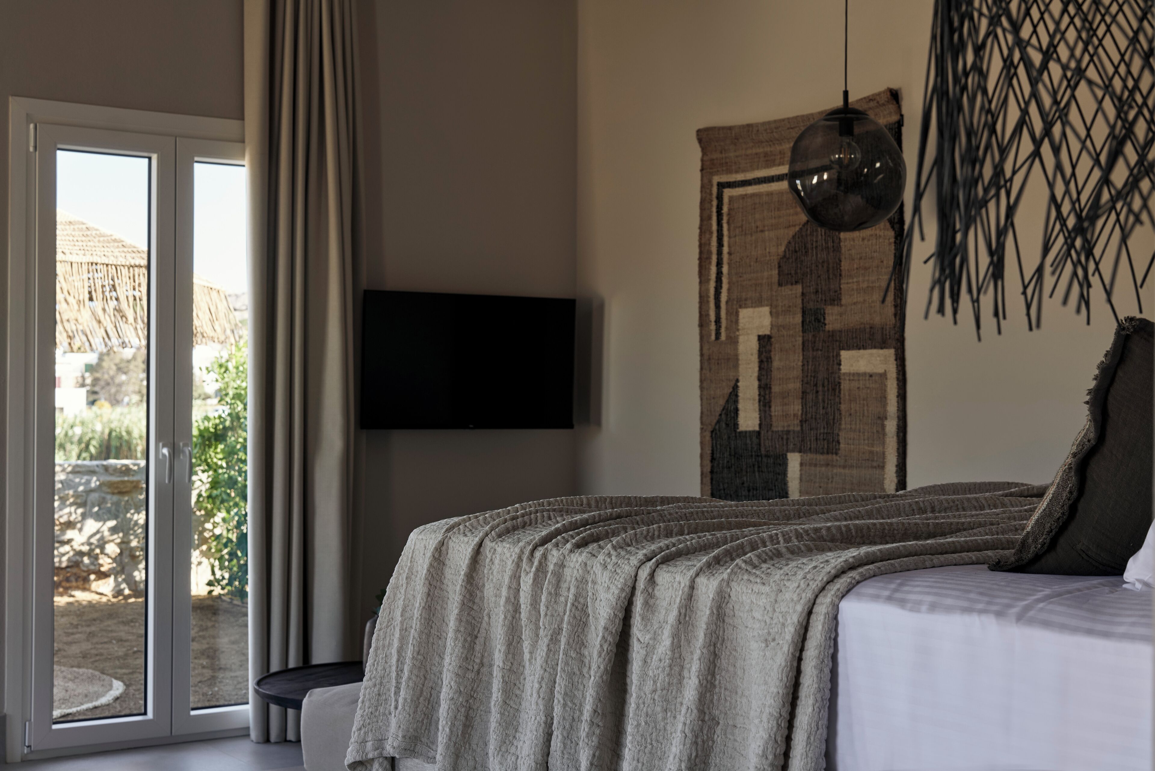 A bedroom with a bed, a TV mounted on the wall, and a view of the outdoors through a sliding door.