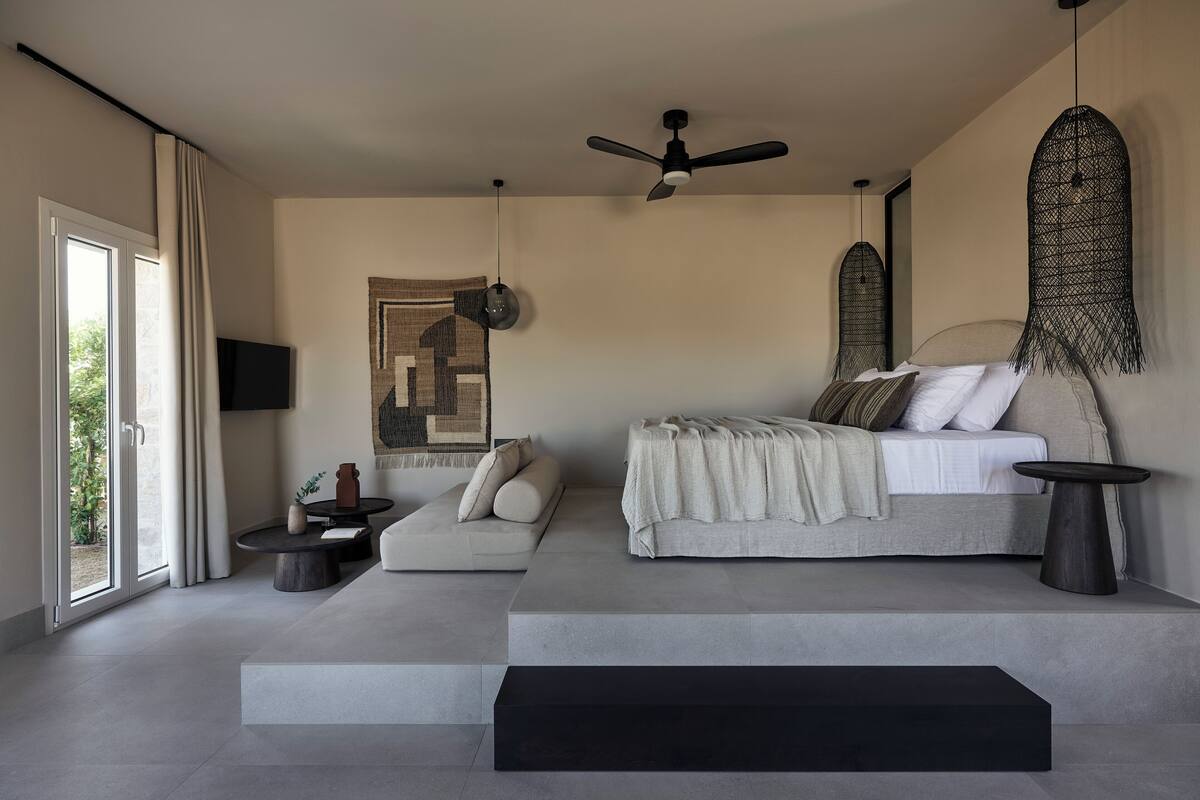 A modern bedroom with a large bed, a sofa, a small table, and a ceiling fan.