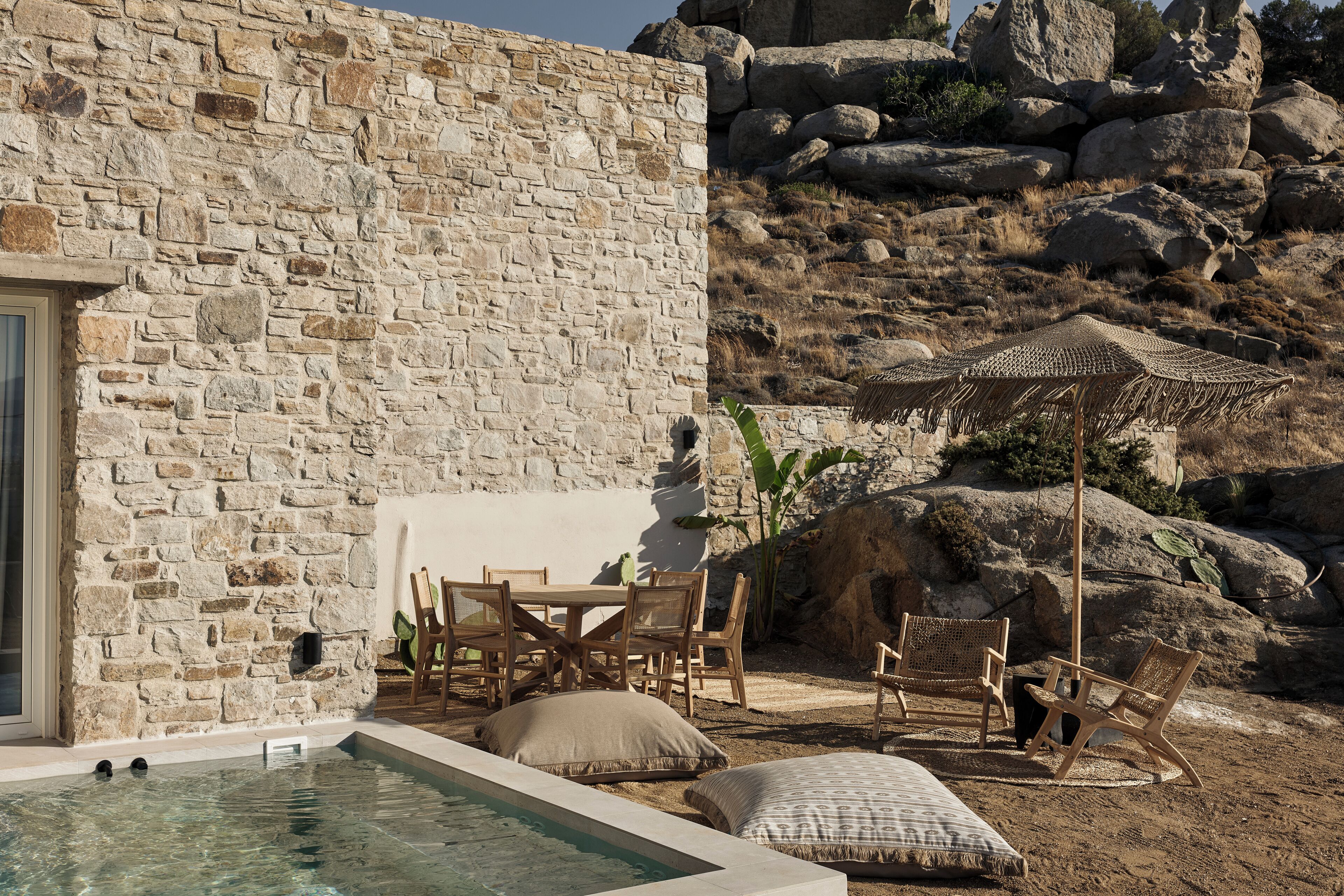 A stone building with a pool, outdoor seating, and a rocky landscape.