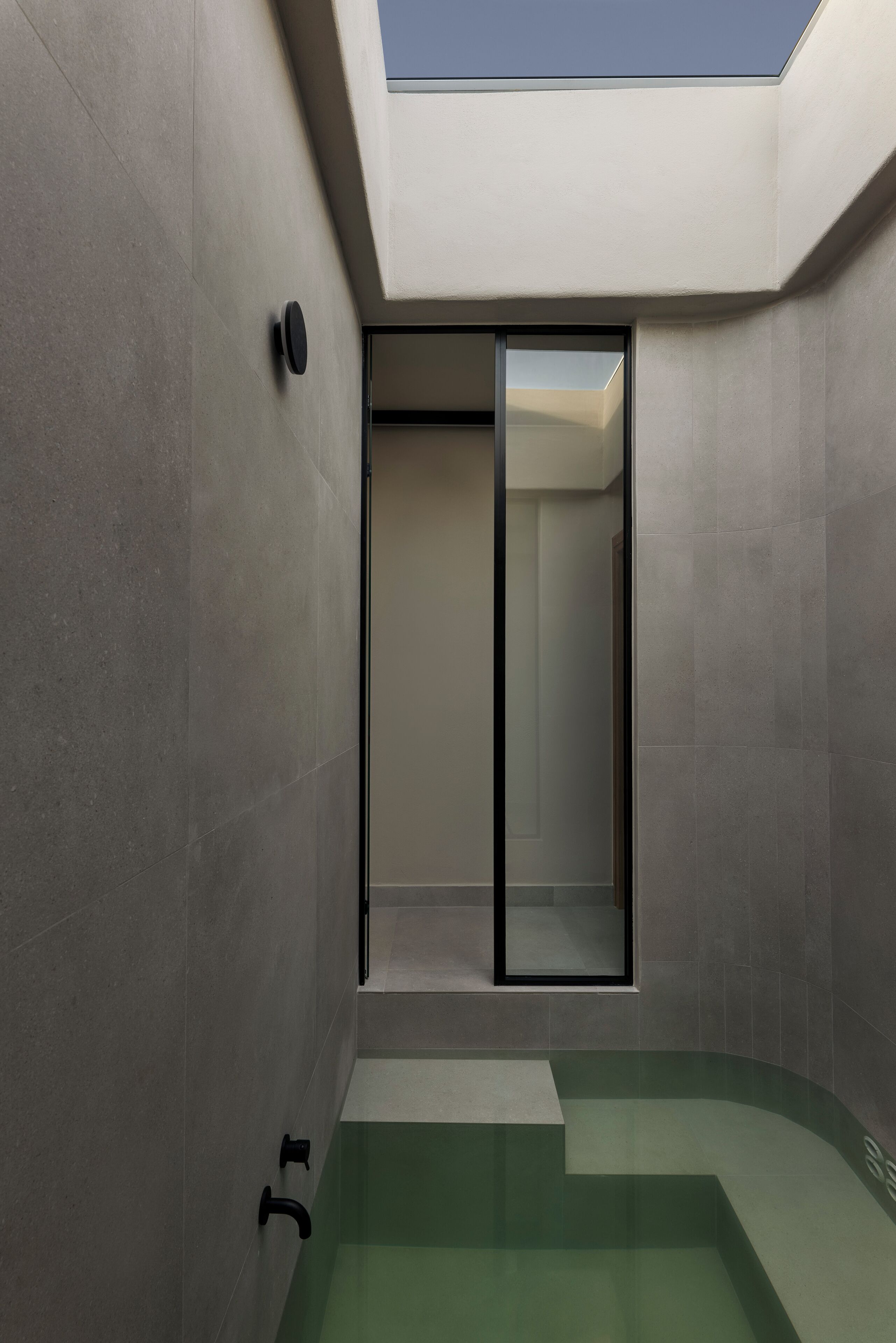 Une salle de bain moderne dotée d’une lucarne, d’une douche en verre et d’une baignoire aux reflets verdâtres.