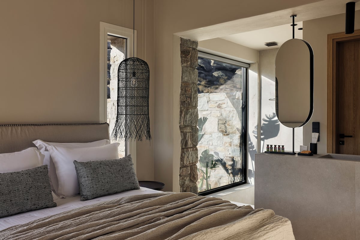 A bedroom with a bed, a large window, a stone wall, and a mirror.