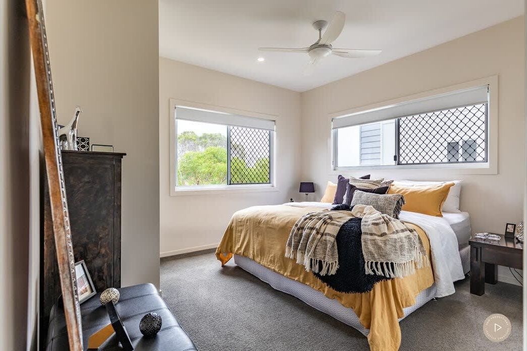 A bedroom with a bed, a ceiling fan, and two windows with blinds.