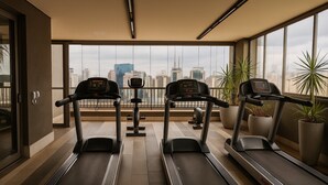 A gym with treadmills and exercise equipment, large windows with a city view, and potted plants. - Elegance Suítes Vergueiro (São Paulo)