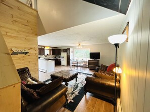 A spacious living room with a high ceiling, a fireplace, and a view into the kitchen area. - Newly Remodeled home with Class A Trout Stream (Austin)
