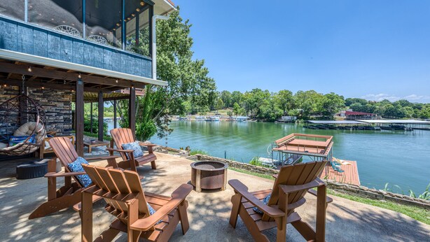 Eine Terrasse am Seeufer mit Adirondack-Stühlen, einer Feuerstelle und Blick auf Boote auf dem Wasser.