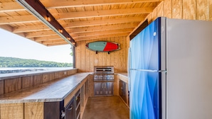 Eine kleine Küche mit Holzbalkendecke, einem Einbauofen, einem Kühlschrank und einem Fenster mit Blick auf ein Gewässer.