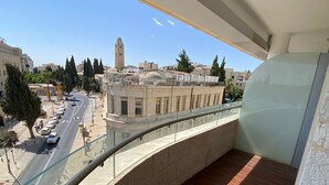 Un balcon doté d’une balustrade en verre incurvée, donnant sur une rue animée par la circulation des voitures et bordée d’immeubles.