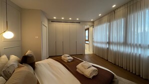Une chambre moderne avec un grand lit, un dressing et une vue sur la ville par la fenêtre.
