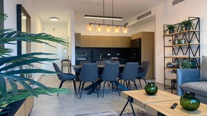 Ein modernes Wohnzimmer mit Essbereich, ausgestattet mit einem Couchtisch aus Holz, einer Couch und einem Bücherregal mit Pflanzen.