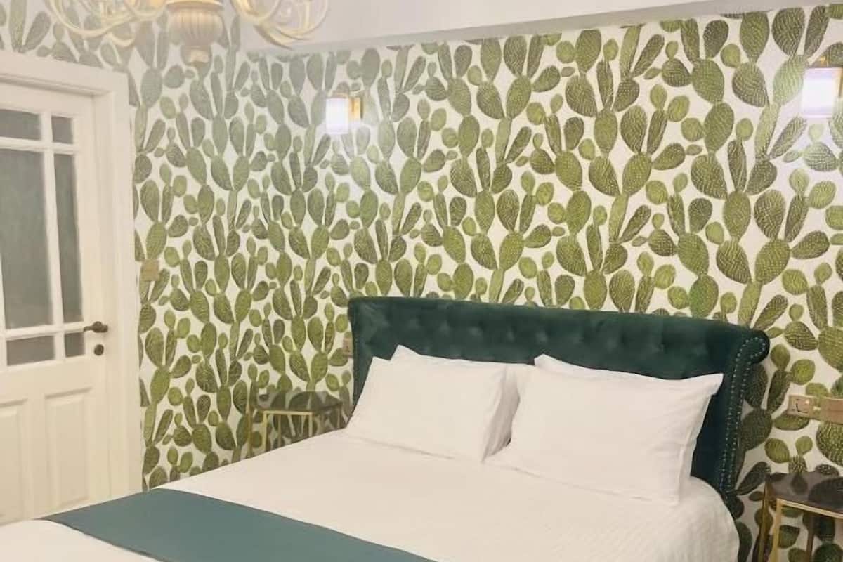 A neatly made bed with a green and white bedspread, a dark green upholstered headboard, and white pillows.