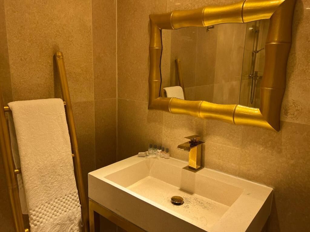 A bathroom with a white sink, gold fixtures, and a mirror with a gold frame.