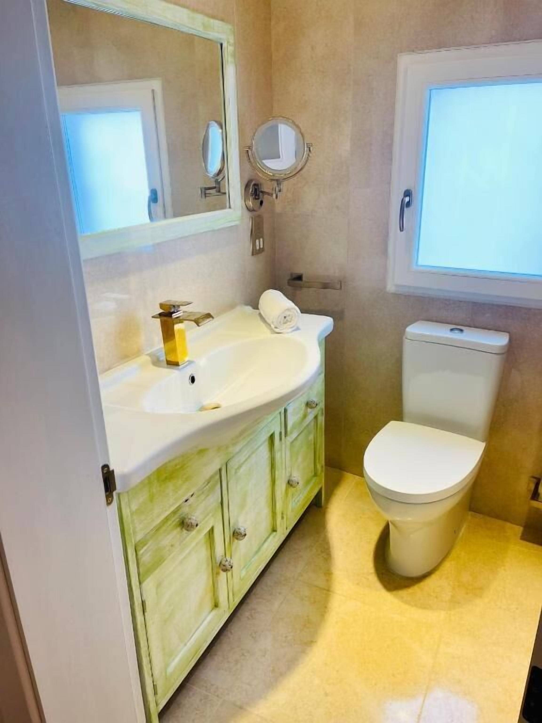 Et badeværelse med en hvid vask, grønne skabe, et toilet og et spejl.