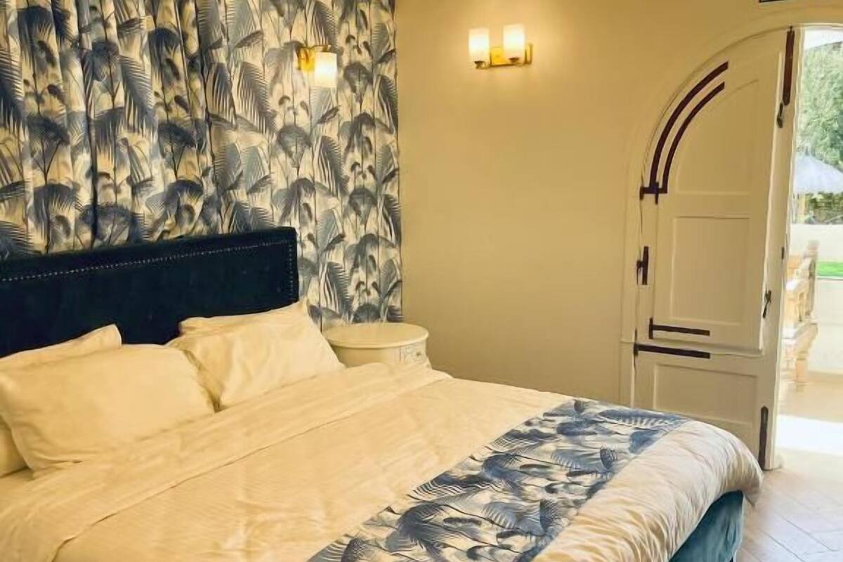 A bed with a patterned headboard, a bedside table, and a wall-mounted light fixture.
