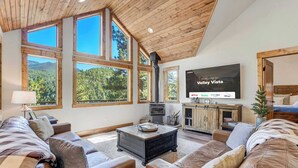 Un salón amplio con ventanas grandes, una chimenea y un televisor de pantalla plana mostrando 'Welcome to Valley Vista'.