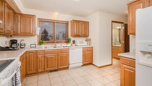 A kitchen with wooden cabinets, a dishwasher, a microwave, and a window with blinds.