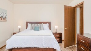 A bedroom with a wooden bed, two bedside tables with lamps, a wooden wardrobe, and a door.