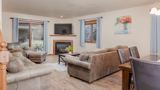 A spacious living room with a fireplace, leather sofas, a dining table, and a TV mounted above it.