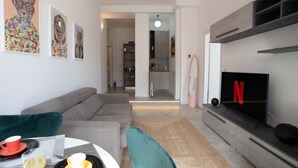 A modern living room with a grey sofa, a coffee table with cups and a laptop, a flat-screen TV with a Netflix logo, and a kitchen in the background. - Design Apartment - Central Station (Milano)