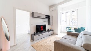 A modern living room with a flat-screen TV, grey sofa, and a large window. - Design Apartment - Central Station (Milano)