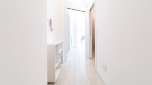 A bright, narrow hallway with a wooden floor and white walls. A phone is mounted on the wall, and there is a door leading to another room. - Design Apartment - Central Station (Milano)