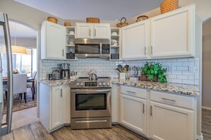A kitchen with white cabinets, stainless steel appliances, and a marble countertop.
