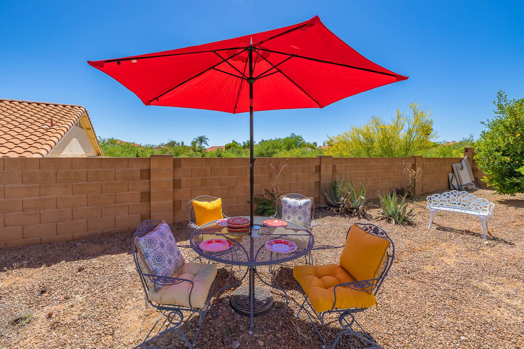An outdoor patio with a red umbrella, metal chairs, and a round table.