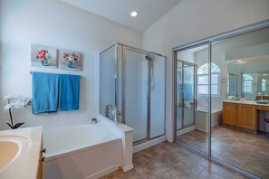 Um banheiro moderno com chuveiro em cabine de vidro, banheira branca e toucador com espelho.