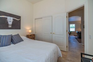 A bedroom with a bed, a nightstand, a lamp, and a door leading to a hallway.